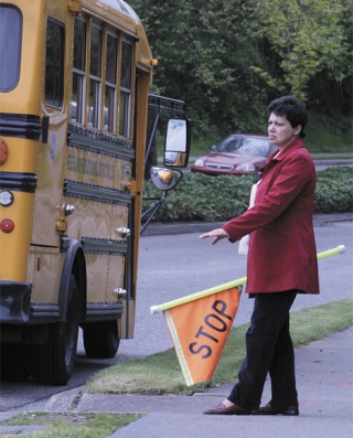 Panther Lake Elementary crossing guard Bev Duncan waves a flag and gives hand motions May 14 to motorists who are speeding through the school zone. The school is one of three that could see speed-detecting cameras replace police patrols by late summer.