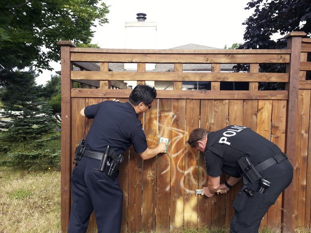 A pair of Federal Way police officers - Deputy Chief Andy Hwang and Lt. Casey Jones -  remove graffiti from Nancy Tabor's fence in the 1800 block of SW 325th Place.