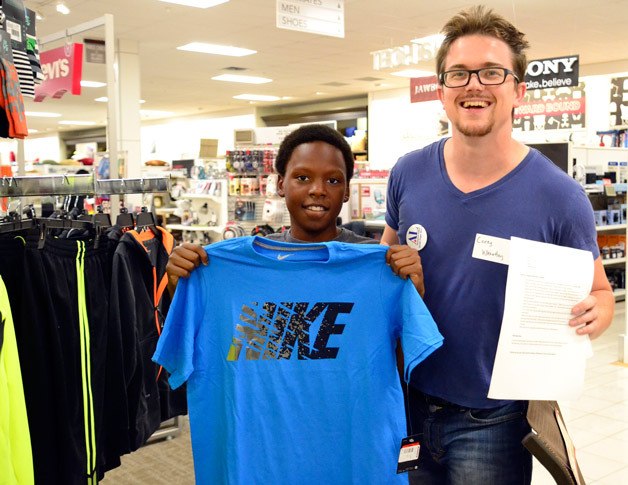 A Sequoyah Middle School student holds up one of the shirts he picked out as a volunteer with the Assistance League of South Puget Sound looks on.