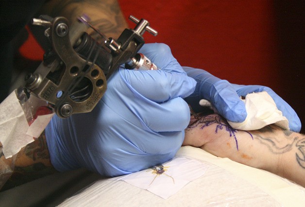 Jose Camarillo’s tattoo needle buzzes away as he performs cover-up work on apprentice Scottie Stopka’s thumb.