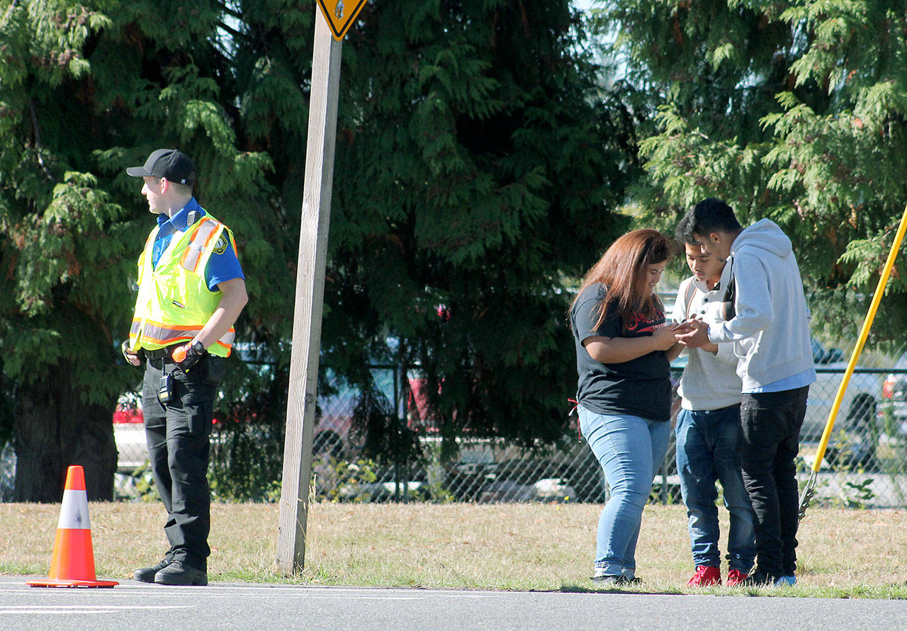 A Federal Way Public Schools campus security officer monitors an entrance into Federal Way High School as students look at a cell phone while waiting to return to school Oct. 3 after a stabbing took place. Mirror file photo