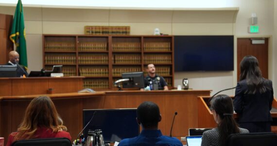 Corniche Washington is in the middle, wearing a blue shirt between his counsel, while prosecutor Jacqueline Lawrence speaks to an officer who responded to the scene. Photo by Joshua Solorzano/The Mirror