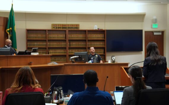 Corniche Washington is in the middle, wearing a blue shirt between his counsel, while prosecutor Jacqueline Lawrence speaks to an officer who responded to the scene. Photo by Joshua Solorzano/The Mirror