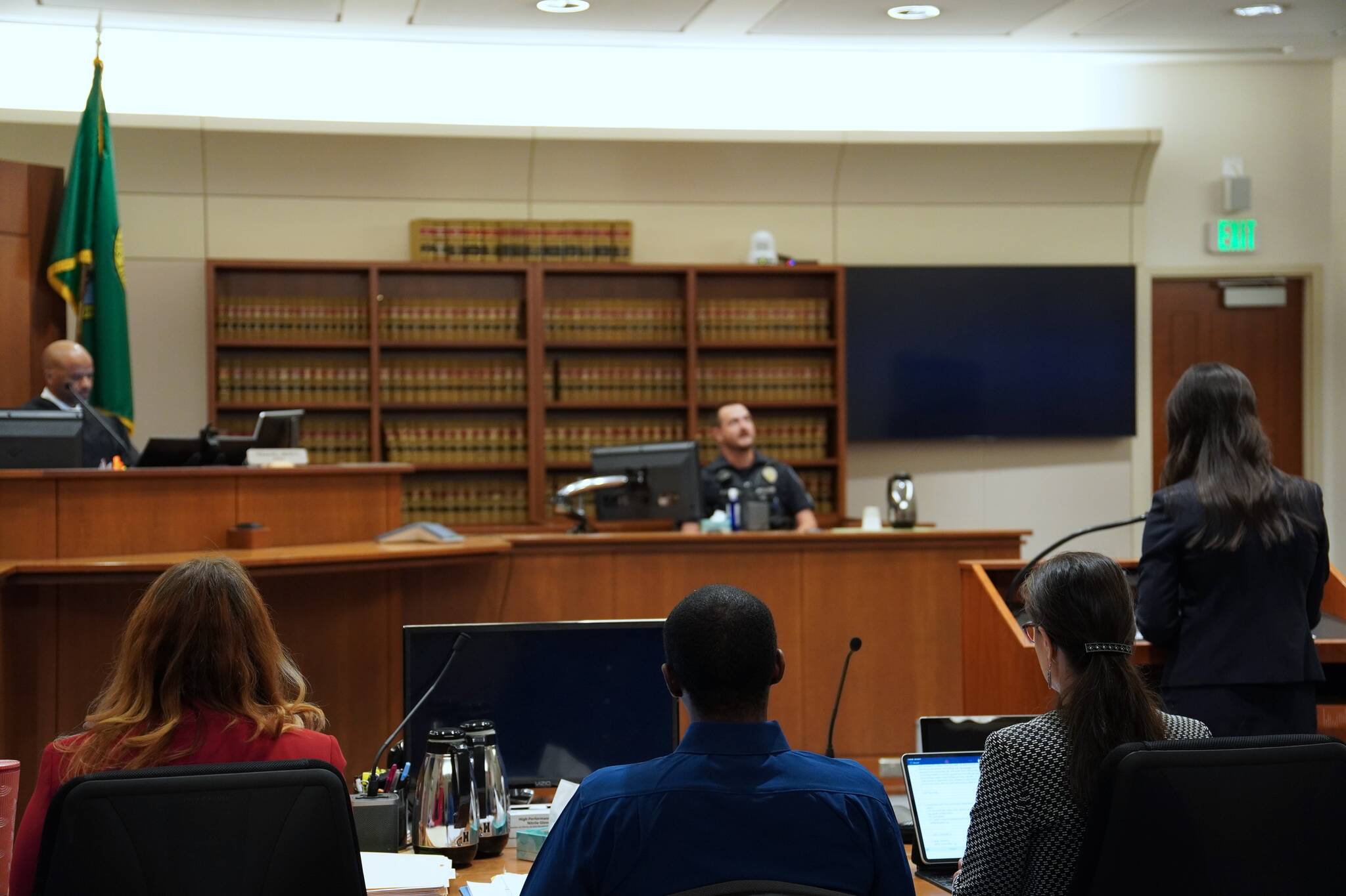 Corniche Washington is in the middle, wearing a blue shirt between his counsel, while prosecutor Jacqueline Lawrence speaks to an officer who responded to the scene. Photo by Joshua Solorzano/The Mirror